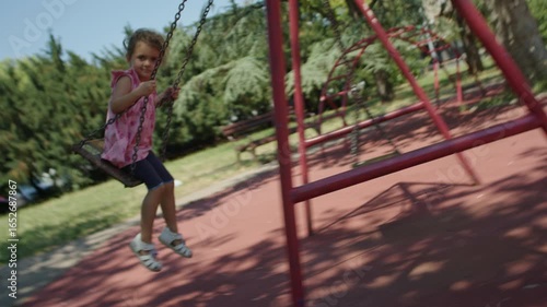 Young girl swinging at public park. Moving cam footage