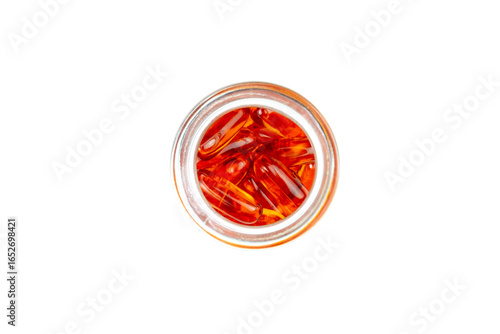 An overhead shot of a clear glass jar filled with red, translucent softgel capsules, isolated on a clean white background, depicting health, medicine, and nutrition.