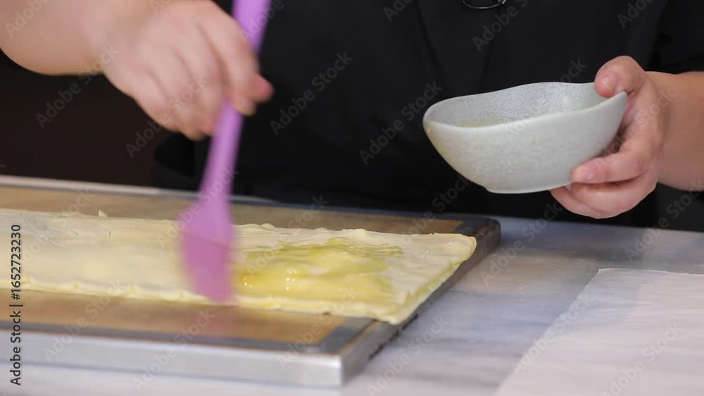 A chef uses a pastry brush to apply an egg wash to a dough topped with dried fruits. This prepares the pastry for baking. A chef uses a pastry brush to apply an egg wash to a dough topped with dried fruits. This prepares the pastry for baking.