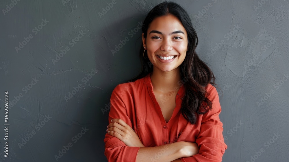 Fototapeta premium Portrait of a young latin woman with pleasant smile and crossed arms isolated on grey wall with copy space. Beautiful girl with folded arms looking at camera against grey wall. Cheerful hispanic woman