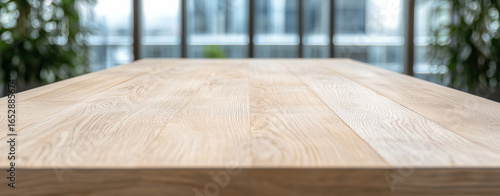 Smooth wooden table surface with natural finish, set in modern interior space filled with greenery and large windows, creates serene atmosphere