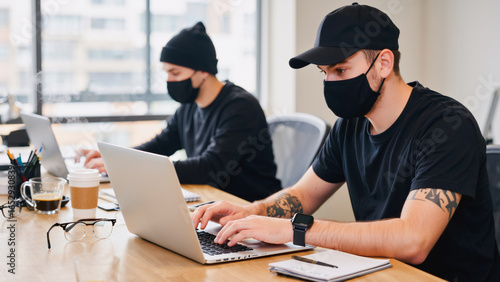 Collaborative Workspace — Suspicious Characters in Disguise, Two men dressed like thieves, appearing as scammers or criminals, diligently working together at a large wooden table in a modern.
