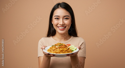 Happy Asian Woman Presenting a Plate of Noodles