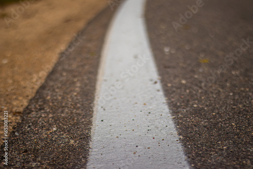 Detailed view of a white painted road marking on textured asphalt with shallow depth of field and blurred roadside gravel.