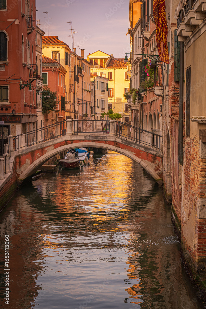 Obraz premium Venetian canal with stone pedestrian bridge at sunset