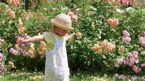Child girl in a blooming garden with bushes of roses and flowers
