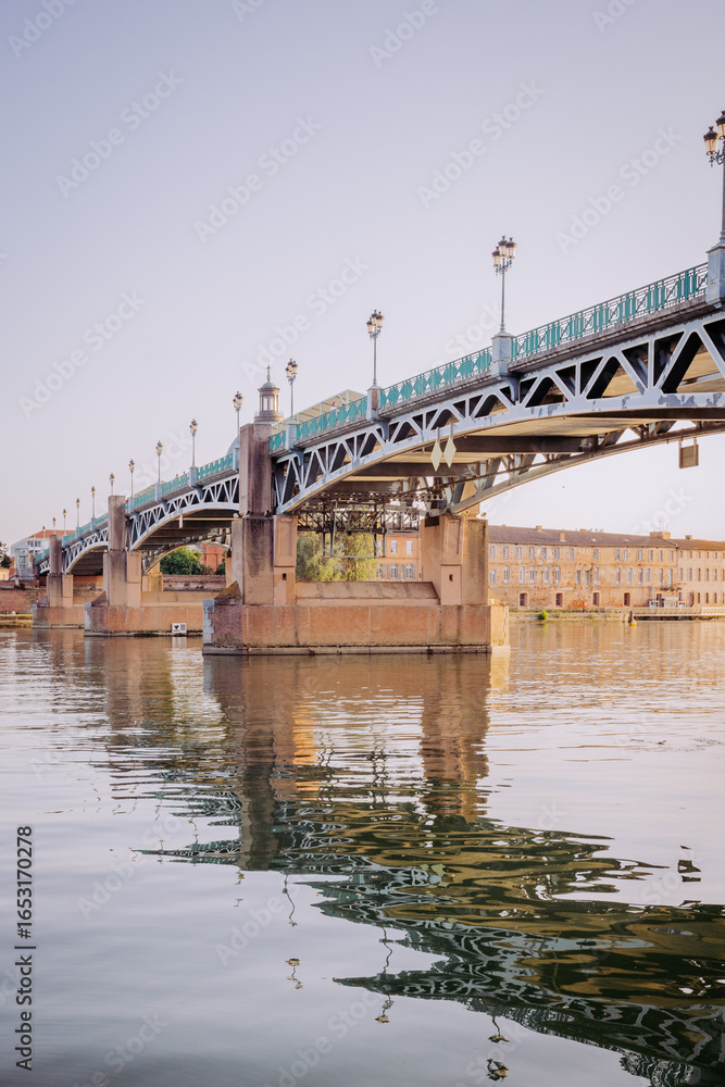 Obraz premium Pont Saint-Pierre à Toulouse, France, au-dessus de la Garonne, avec reflets dans l’eau au coucher du soleil.