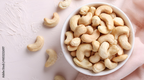Bowl full of cashew nuts on a textured surface with a delicate pink fabric, showcasing healthy snack.