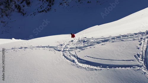 Snowboarder leaving s-shaped trail on snowy mountain slope