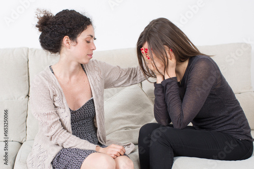 A young woman offers comfort to her distressed friend hiding her face in her hands, symbolizing grief, trauma, empathy, and psychological support in difficult times.