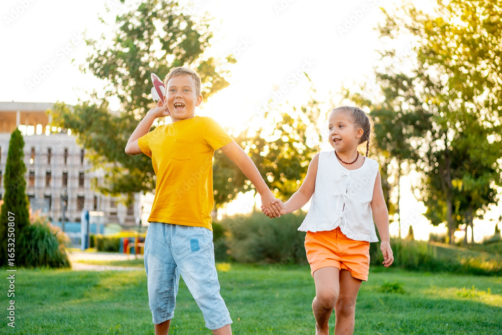 Obraz premium little children flying a plane, a boy and a girl playing with a plane on a green lawn, laughing children on the grass in summer, summer holidays