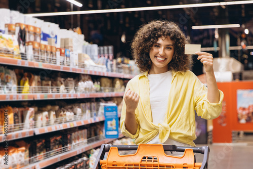 Woman pushing shopping cart and showing fidelity card in supermarket
