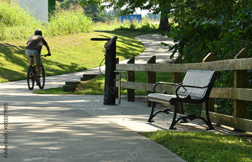Paved walking trail with bench, cyclist, and bike repair station