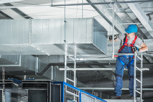 Construction HVAC Worker Installing Air Duct in Warehouse During Daylight Hours
