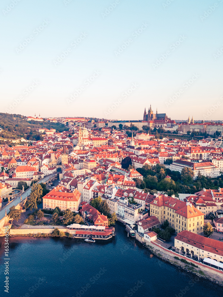 Fototapeta premium Golden light illuminates the city of Prague at sunrise, casting a warm glow over the medieval buildings, the Vltava River, and the iconic Charles Bridge, creating a breathtaking morning panorama.