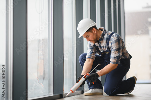 Construction worker sealing window frame with silicone gun in modern building