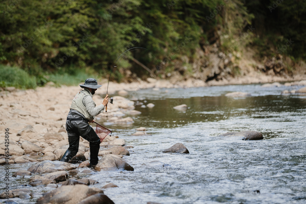Fisherman catching trout in river, fly fishing in mountain stream Fisherman catching trout in river, fly fishing in mountain stream
