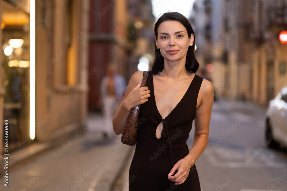 Fototapeta premium In evening, woman walks along narrow street between buildings of 19th century, gets acquainted with everyday life of city. Streets and avenues of Barceloneta. Pedestrian in summer European capital.