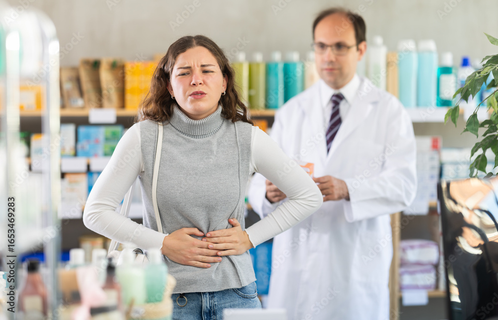 Fototapeta premium Young woman suffering from stomach pain. Male pharmacist offering stomach pain pills