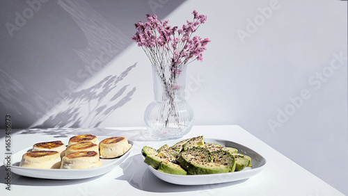 Elegant Food Still Life Pancakes, Avocado Slices, and Floral Vase on White Surface