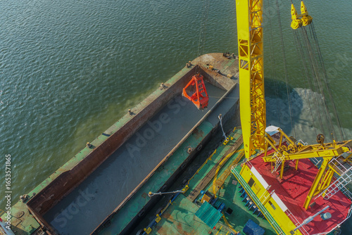 Drone photo showing a crane barge lifting dredged material into a barge during marine maintenance to keep waterways navigable