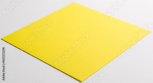 A square of yellow paper placed diagonally on a white surface in a studio setting with soft lighting on transparent background