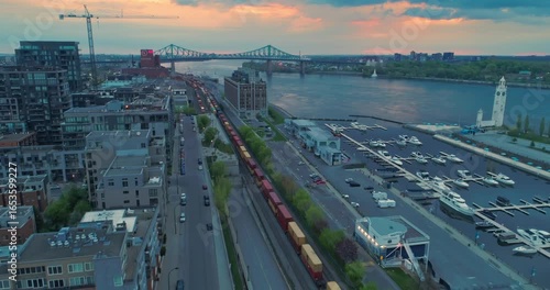 Aerial view of Montreal, Canada, featuring the Jacques Cartier Bridge, a train, and a marina at sunset. The photo captures the city's infrastructure and waterfront.