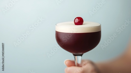 Elegant dark cocktail with creamy foam and cherry garnish