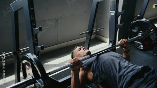A man engaging in a bench press workout at the gym. He is lifting heavy weights for strength training, promoting fitness and muscle growth. Dedication and effort shown in his expression.