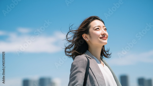 青空の下で都会を背景に立つ爽やかなビジネスウーマン「生成AI」