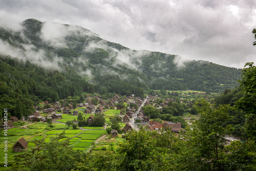 Fototapeta premium Traditional Shirakawa-go village in summer rain with rice fields and misty mountains