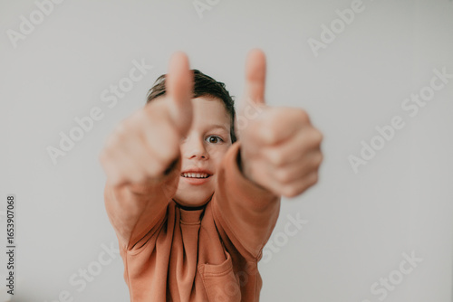 A preschool boy on a light background shows a thumbs up