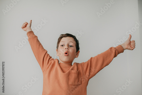 A preschool boy on a light background shows a thumbs up