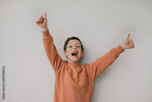 A preschool boy on a light background shows a thumbs up