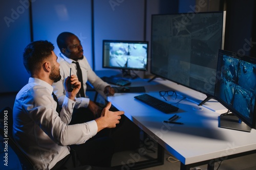 Fotografie Two male security guards looking at computer screen while one of them explaining