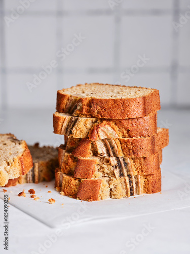 Freshly baked banana bread is sliced and neatly stacked on a white surface, showcasing its inviting texture and delightful aroma, perfect for a breakfast treat or snack