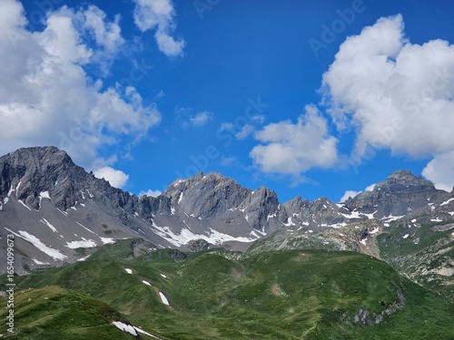 La Thuile, Val D'Aosta, July 02 2025: Panoramic view to the alps, beautiful green landscape reflected in a small natural lake. Beautiful blue sky with some clouds. Mountains with a little snow. Aerial