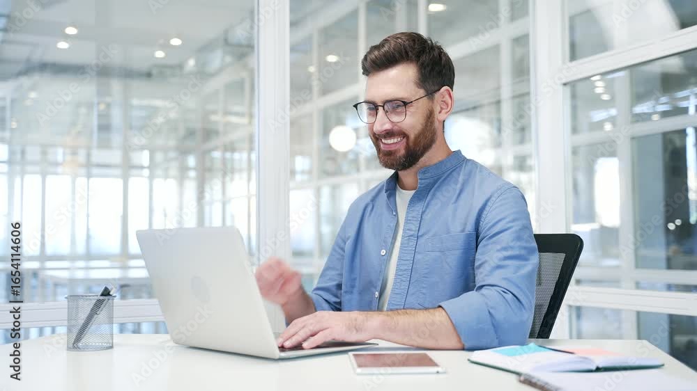 Satisfied happy businessman received great news on laptop while sitting at a desk at workplace in modern business office. Smiling glad handsome entrepreneur reads a positive good message on a computer Satisfied happy businessman received great news on laptop while sitting at a desk at workplace in modern business office. Smiling glad handsome entrepreneur reads a positive good message on a computer