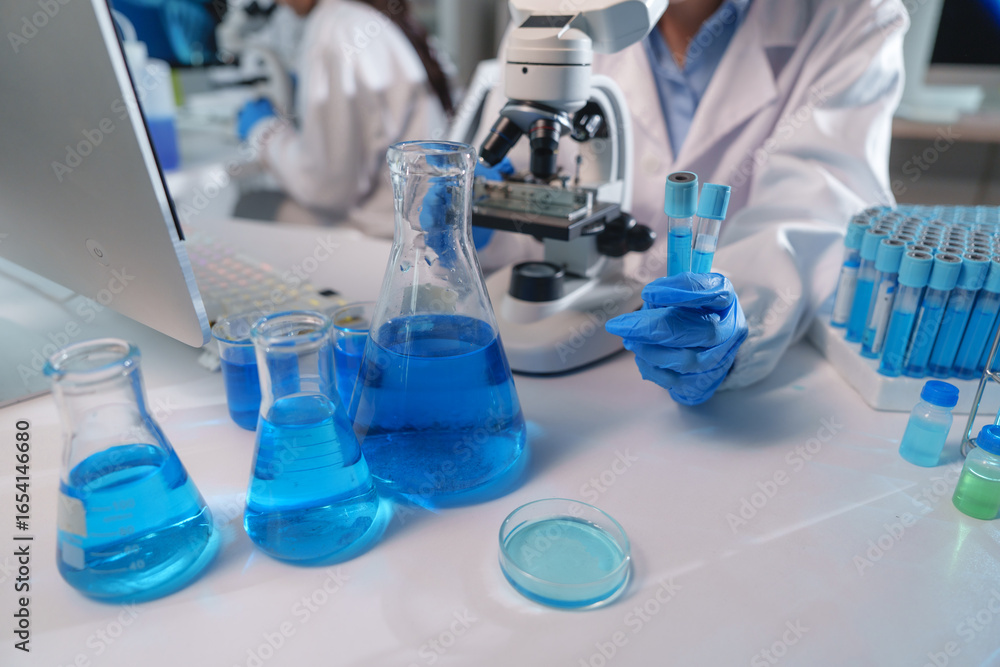 Fototapeta premium Scientist holding test tubes with blue liquid in laboratory