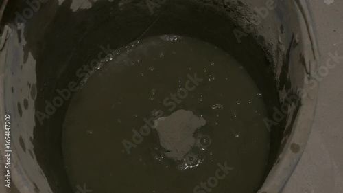 Pouring concrete mixture into water-filled bucket, stirring for optimal consistency and preparation process. pouring concrete mixture into bucked with water 