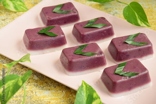 
Indonesian traditional cake Kue Talam Ubi Ungu served on a plate. It is made of a rice flour, coconut milk and other ingredients, garnish with pandan leaves. Indonesian dessert