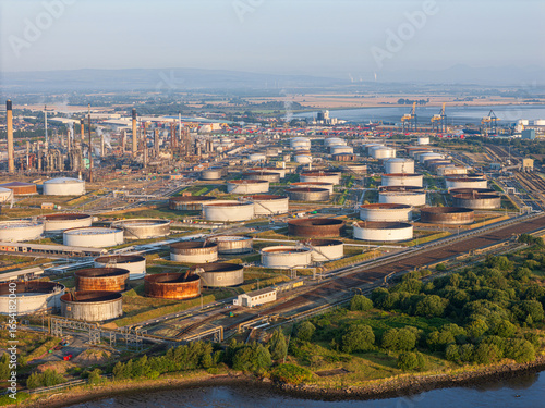 Aerial view of a sprawling industrial landscape with cylindrical tanks contrasting against lush greenery and the winding river, Grangemouth, Scotland, United Kingdom.