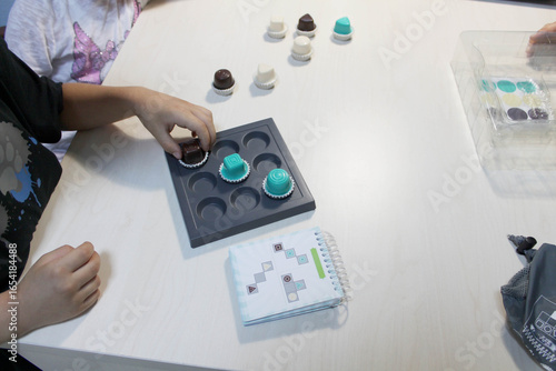 Board game, a visual perception exercise for visual therapy. Pieces of different colors and shapes are placed on the board according to rules. Children's hands playing a board game with pieces.