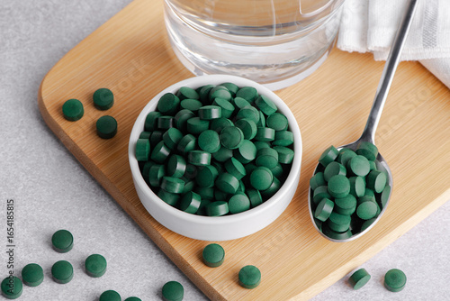 Spirulina powder and tablets in the bowl. Spirulina algae powder and tablets on gray background
