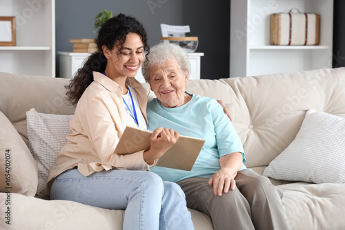 Young African-American female medical worker reading book with elderly woman ...