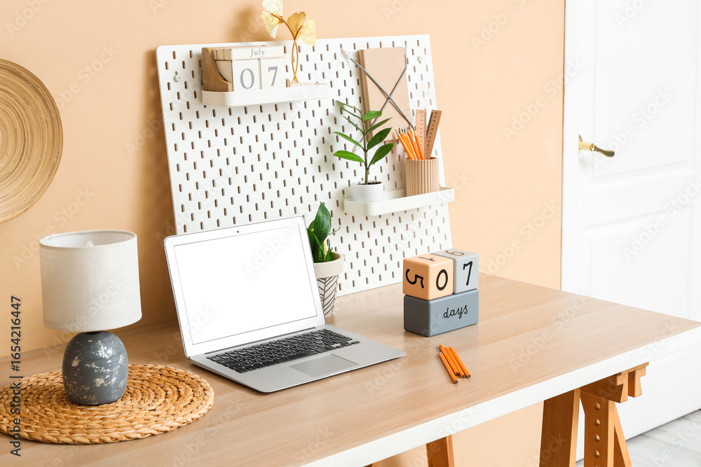 Obraz premium Stylish workplace with modern laptop, cube calendars and pegboard near color wall