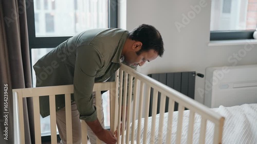 A man stands and assembles a crib while a pregnant woman sits on the bed next to him
