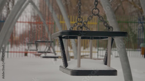 Snow gently blankets the urban playground, transforming swings and slides into winter wonders. Children will enjoy this magical scene once the snowfall stops.