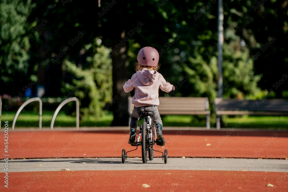 Obraz premium Child cycling on small bicycle with training wheels in park, helmet for safety, practicing balance, outdoor play, active lifestyle, childhood development, fun exercise, sunny day nature setting