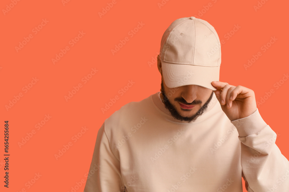 Naklejka premium Handsome young man in stylish cap on orange background